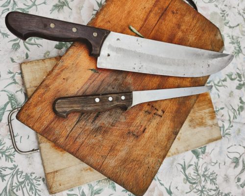 wooden chopping board with kitchen knives, placed on an old flower tablecloth, photograph with a view from above